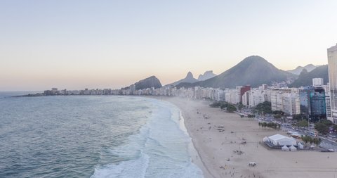 Aerial hyperlapse of dusk at Copacabana beach in Rio de Janeiro. Movement of waves in the ocean, people at the beach and cars at the avenue. Brazil