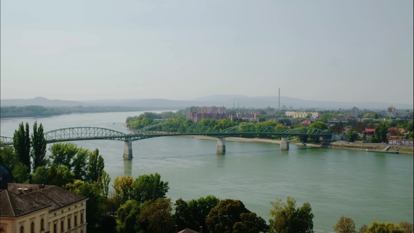 Timelapse of Danube and Mária Valéria bridge. Traffic in the bridge. Slight smog and factory chimney in the distance. Group of block houses.