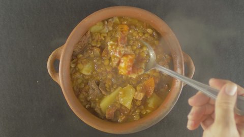 TOP VIEW Stew of Brown lentils Tradicional Spanish dish Lentejas in a clay pot with smoke, stable close up with potatoe, carrot, meal, onion, garlic grains Served with spoon