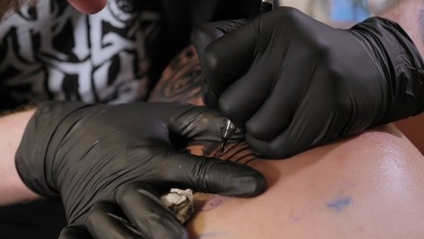 Close-up of a tattoo artist doing a tattoo on the leg of a young girl in the salon. Professional tattooist doing tattooing in studio. Skin art close-up. Slow motion.