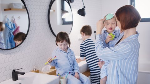 Mother with small children in pajamas in bathroom at home, brushing teeth.