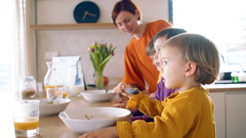 Mother with small children in kitchen in the morning at home, eating breakfast.