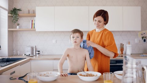 Mother with children in kitchen in the morning, getting dressed when eating breakfast.