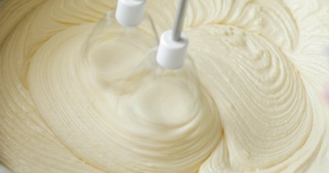 Baker is mixing ingredients electric mixer in bowl pouring milk cooking dough for cake, closeup view. Steps of baking and confectionery. Preparing sweet food dessert in kitchen. White creamy dough.