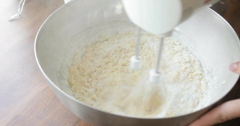 Baker mixing ingredients in bowl cooking dough baking cake using electric mixer, closeup view. Steps of baking and confectionery. Preparing sweet food dessert in kitchen at home on wooden table.