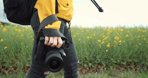 Close up of female photographer in casual outfit carrying on her camera while walking on green wheat field. Mature woman taking pictures of beautiful nature around.