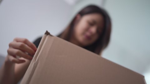Asian woman unboxing cardboard package, woman parcel box opening, online shopping delivery, unpacking package sit on sofa at home, blur background, look up shot, new normal life style, home quarantine
