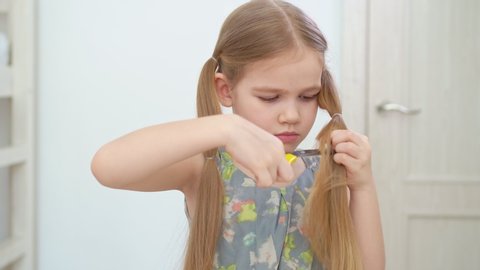lifehack haircut caret. Cute little girl cutting long blond hair to herself with scissors, funny look, indoor portrait. haircut at home.