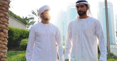 Two young businessmen going out in Dubai. Friends wearing the kandura traditional male outfit walking in Marina