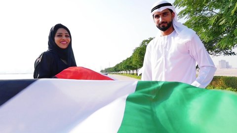 Couple spending time together in Dubai. Man and woman wearing kanura and hijab walking near the ocean and watching the skyline