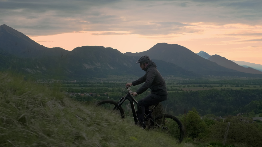 Close up shot of young athletic man on MTB e-bike pedaling up the hill in the morning. Sun is waking up. Good outdoor sport for health.
