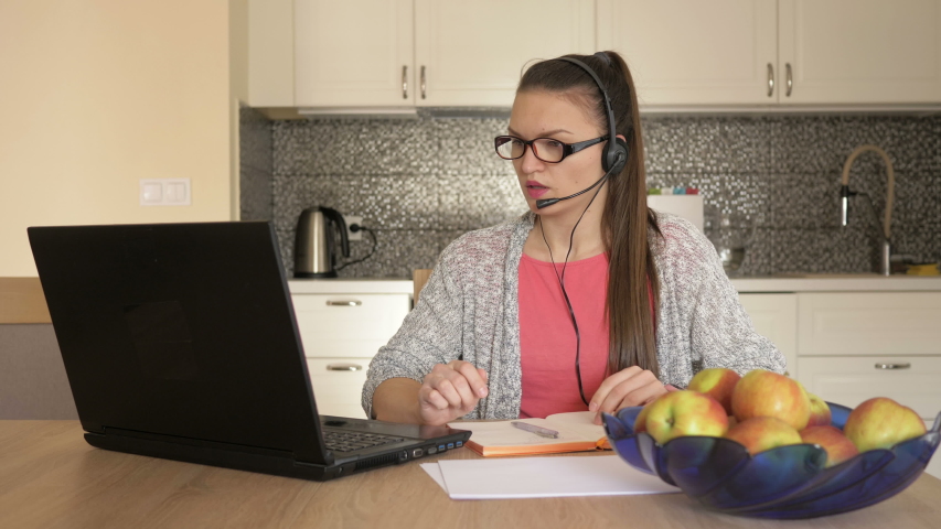 Young woman with headset in front of laptop at the table, online customer consultation.