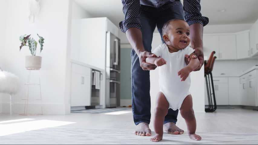 Close up of father encouraging smiling baby son to take first steps and walk at home - shot in slow motion Royalty-Free Stock Footage #1053167303