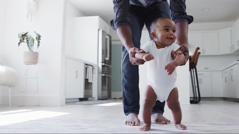 Close up of father encouraging smiling baby son to take first steps and walk at home - shot in slow motion