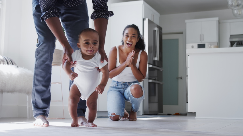 Close up of parents encouraging smiling baby son to take first steps and walk at home - shot in slow motion | Shutterstock HD Video #1053167312