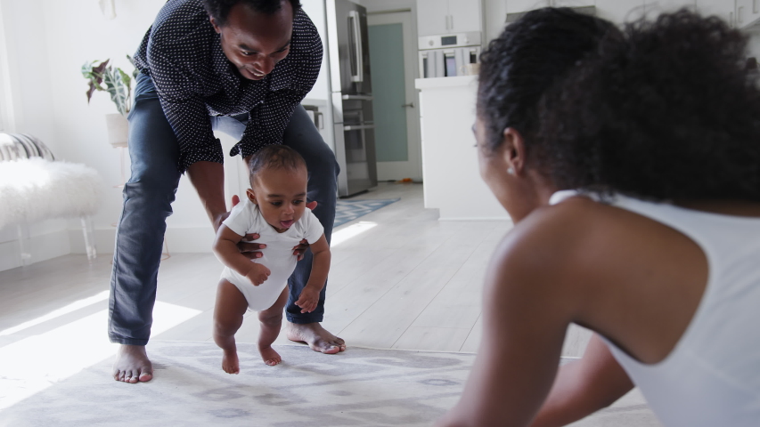 Close up of parents encouraging smiling baby son to take first steps and walk at home - shot in slow motion | Shutterstock HD Video #1053167333