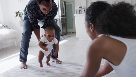 Close up of parents encouraging smiling baby son to take first steps and walk at home - shot in slow motion