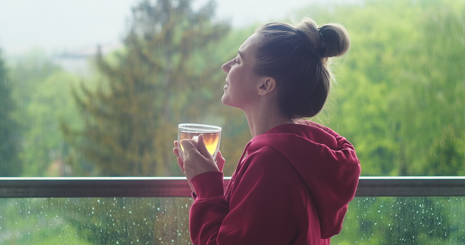 Woman drinks tea, and relax on terrace at home. Rain, fresh air. Social distancing, stay at home. 4K Video | Shutterstock HD Video #1053168911