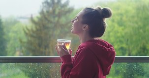 Woman drinks tea, and relax on terrace at home. Rain, fresh air. Social distancing, stay at home. 4K Video