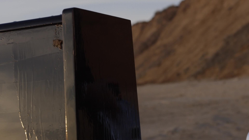 Man on the beach pours old piano gasoline from a metal canister, prepares to set fire. art scene