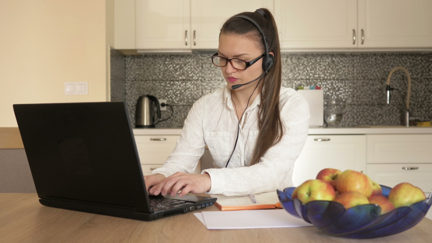 Woman with headset in front of laptop at the table, online consulting. Telework.