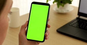 Back view of brunette holding chroma key green screen smartphone watching content. Gadgets and contemporary people concept