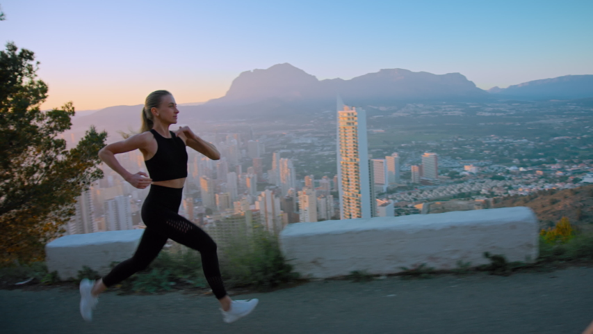 Cinematic epic shot of incredible fit and strong young woman run to success on morning workout at sunrise or sunset. Amazing inspiring and motivational female runner during interval sprint over city Royalty-Free Stock Footage #1053175838