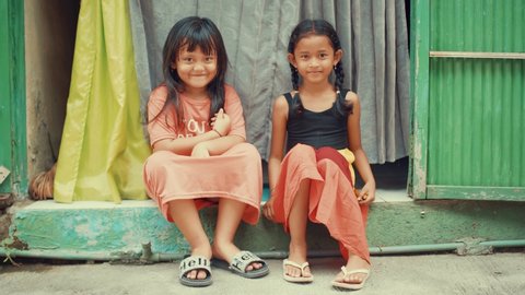 Ubud , Bali Indonesia / Indonesia - 10 14 2019: Two young girls are sitting outside them house. They are shy and smiling. Very colourful environment around.