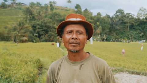 Ubud , Bali / Indonesia - 10 23 2019: Portrait of Balinese farmer man in the middle of rice field. Forest and others workers on the background