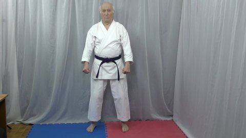 On red and blue tatami old man athlete is training formal karate exercises