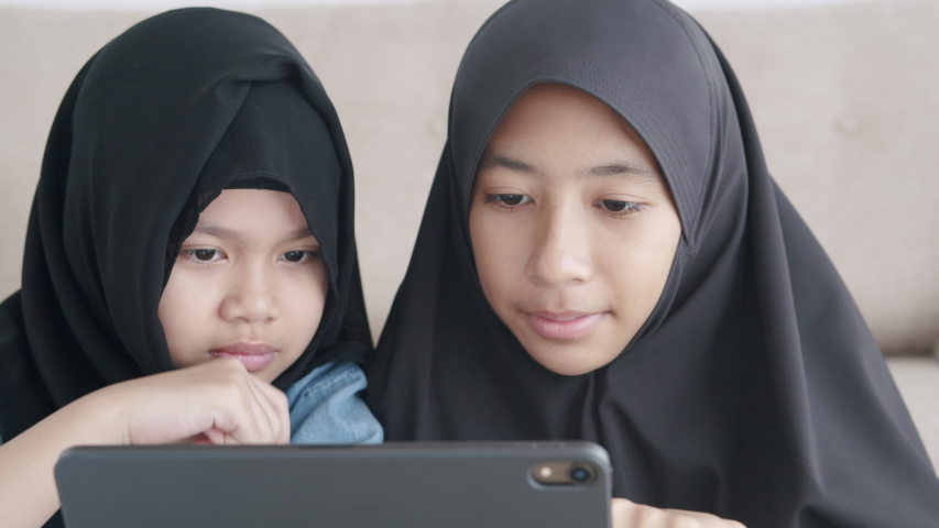 Two Muslim girl is studying online via the internet on tablet in living room at home, Asian elementary school children watching computer tablet. Concept of education at home. Close-up on the face kid Royalty-Free Stock Footage #1053179729