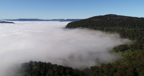 Hill sides of Kangaroo valley and sandstone mountain plateau in morning light with thick cloud cover in elevated aerial flying.

