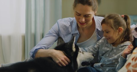 Caucasian mother and daughter sitting on a sofa, playing with pet dog at home. Shot on RED Helium 8k