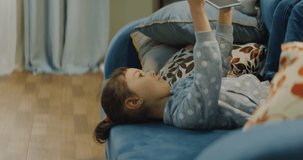 Pre-school Caucasian girl lying on a sofa, playing games or wathcing cartoons on a tablet. Shot on RED Helium