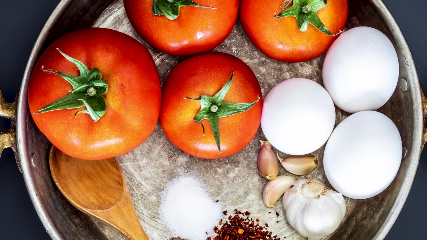Traditional turkish food menemen materials; tomatoes, spices, salt and eggs with wooden spoon in copper pan on background. turning top view