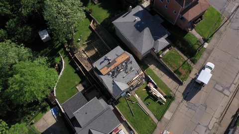 A high orbiting aerial flyover of roofers removing the shingles of a house before laying down a new roof. Pittsburgh suburbs.  	