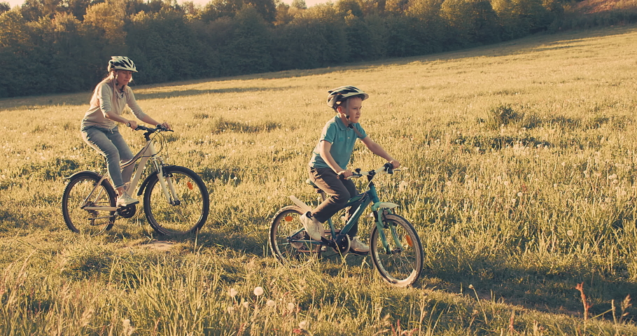 Mother and son ride a bike. Happy cute boy in helmet learn to riding a bike in park on green meadow in summer day at sunset time. Family weekend. 4K video, Slow motion