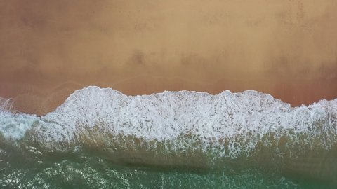 Drone view of beautiful seamless never ending footage while turquiose sea waves breaking on sandy coastline. Aerial shot of golden beach meeting deep blue ocean water and foamy waves. 