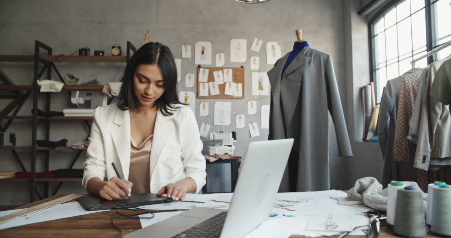 Asian female clothing designer is drawing her sketches on graphics tablet, preparing her new collection - fashion, success concept 4k footage