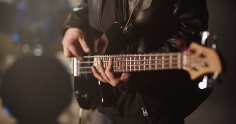 A rock bass guitarist is playing a solo line during performance in club, band mate drummer hitting cymbals on background 4k footage