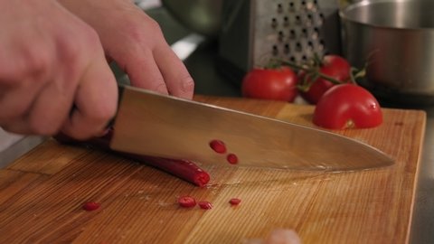 Close-up of a chef slicing hot chili peppers on a chopping Board in a restaurant kitchen. Slow motion.