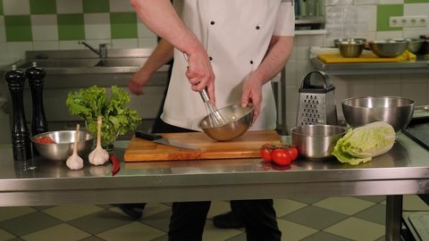 Close-up of a professional chef mixing eggs in a bowl in a modern restaurant kitchen. Preparing an omelet or pizza dough. Slow motion.