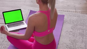 A laptop with a green screen is in front of a young woman meditating. Remote training during quarantine.