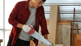 young Asian man wearing protective white  gloves used hand-saw DIY to cut  the wood plank in the workshop recording live streaming on social media. working at home concept   - Powered by Shutterstock - Get 15% off with code: PIKWIZARD15