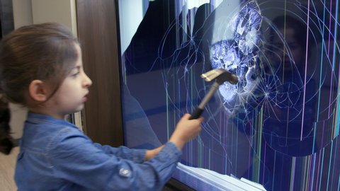 Upset little girl smashing LCD TV set screen with hammer. Angry female child hitting television monitor with heavy object for rage and violence