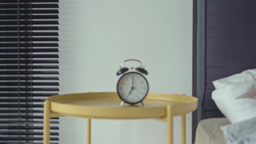 An alarm clock rings in the morning on a bedside table. The girl’s hand overturns the alarm so that he shuts up. Royalty-Free Stock Footage #1053201908