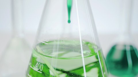 Laboratory flasks with clear liquid and living algae. Hand in a medical glove is dripping liquid into a glass flask. Production of natural cosmetics from marine plants.