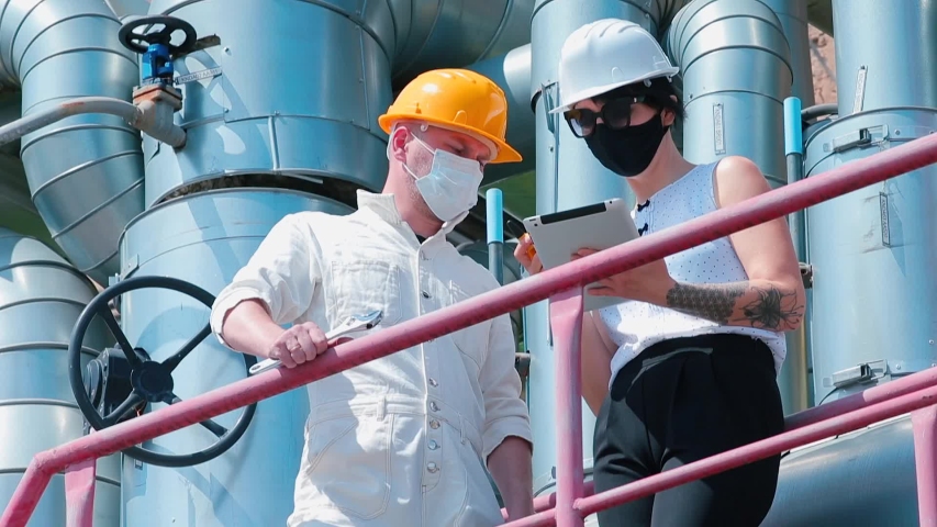 Female manager in a protective mask on face and helmet, talking to a subordinate worker. Gender equality in the choice of special profession. Factory work during the COVID-19 pandemic. Royalty-Free Stock Footage #1053205718