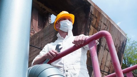 A man in a mask on face and a helmet on his head stands at a construction site. Overhaul and maintenance of buildings and structures during quarantine COVID-19, Omicron wave. Worker stress relaxation.
