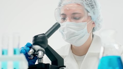 Beautiful female scientist laboratory technician in protective equipment looks through microscope for an fertilization procedure. Concept of modern effective treatments for infertility